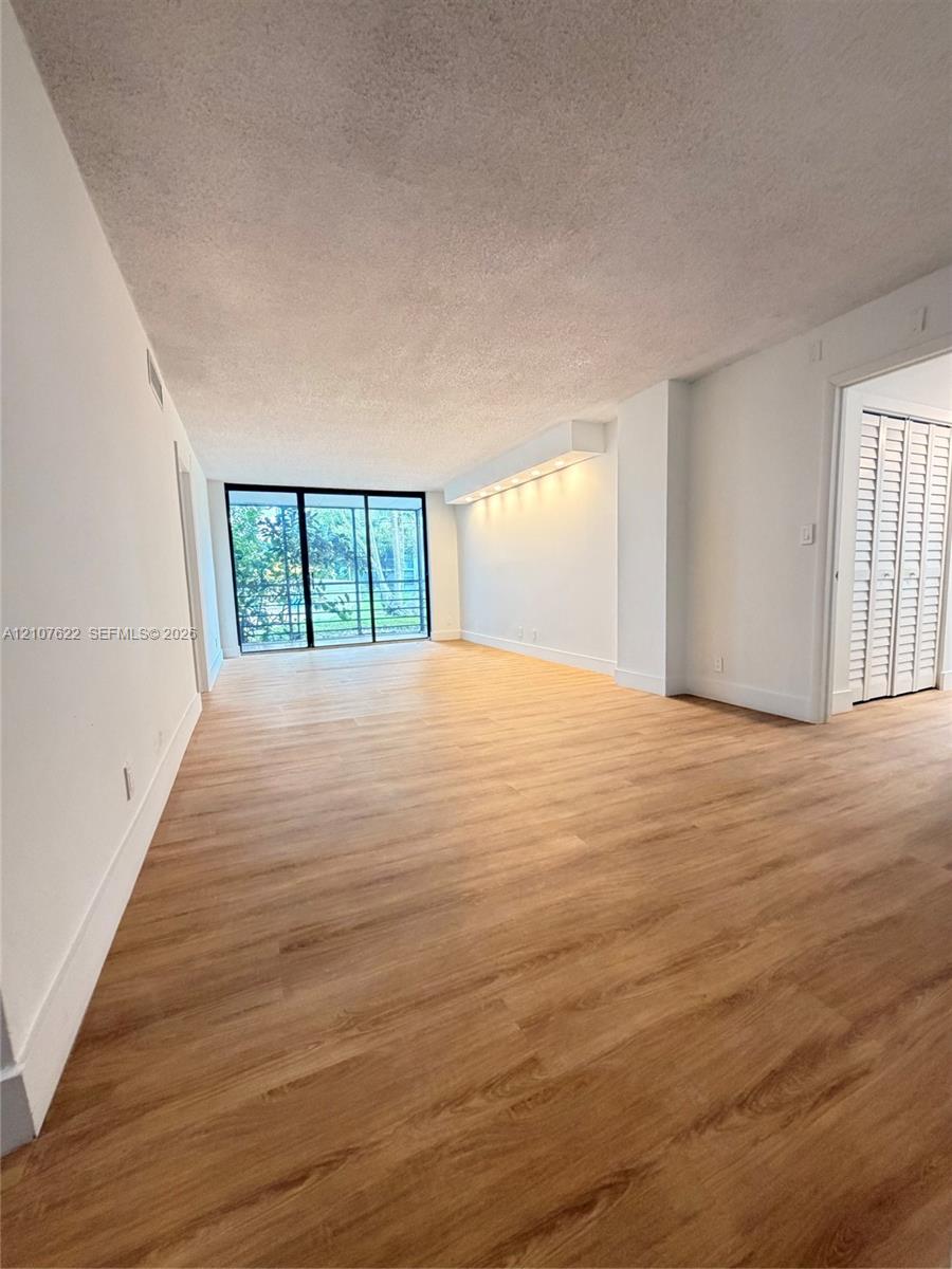 Open-concept room featuring wood-finish flooring, floor-to-ceiling sliding glass doors, built-in recessed soffit lighting, and closet doors with louvered panels
