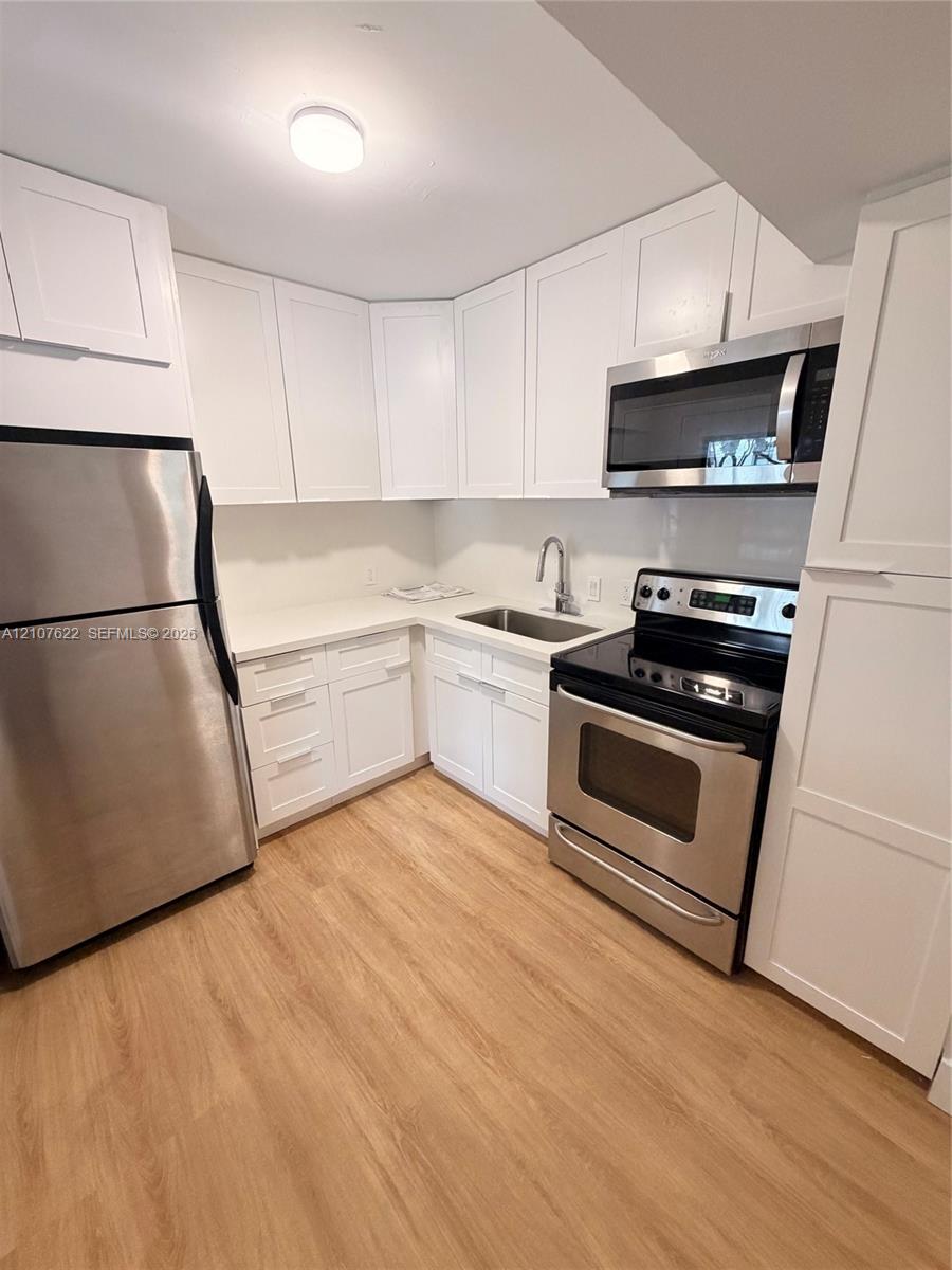 Kitchen featuring white shaker-style cabinetry, solid-surface countertops, stainless steel appliances, and wood-finish flooring