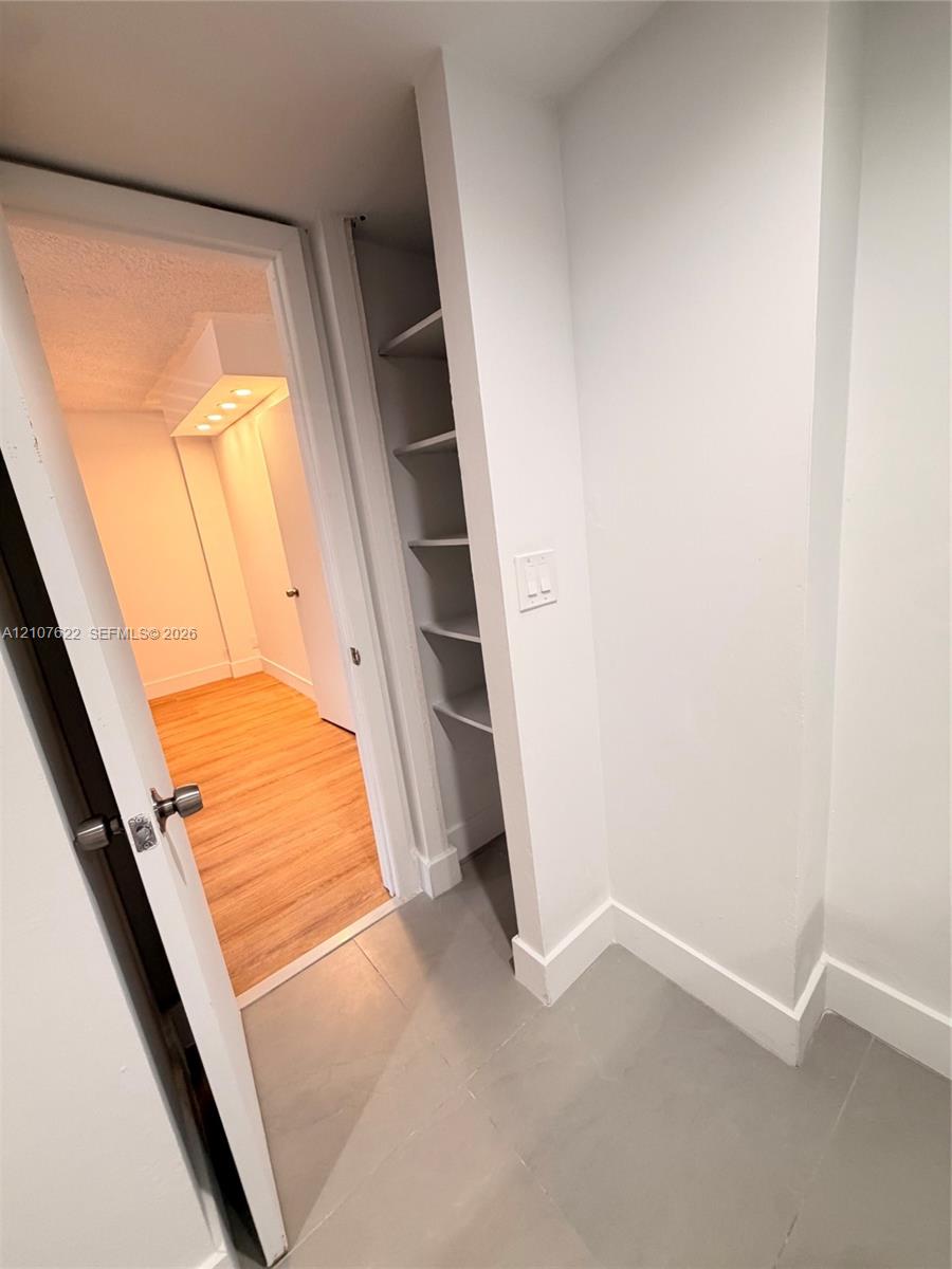 Interior space featuring large-format ceramic floor tile, built-in recessed shelving, and a wood-finish floor beyond a doorway with brushed metal hardware