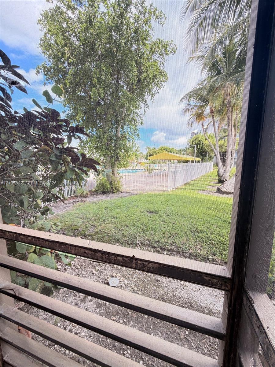 Screened enclosure overlooking a grass lawn, mature palm trees, perimeter fencing, and a swimming pool