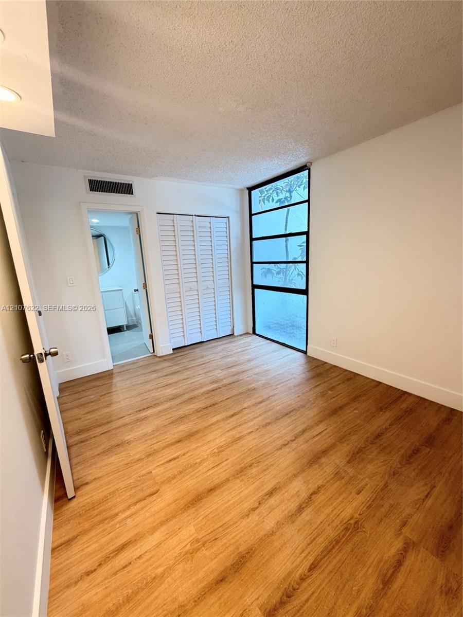 Wood-finish flooring, floor-to-ceiling multi-panel fixed window, and white louvered-style closet doors