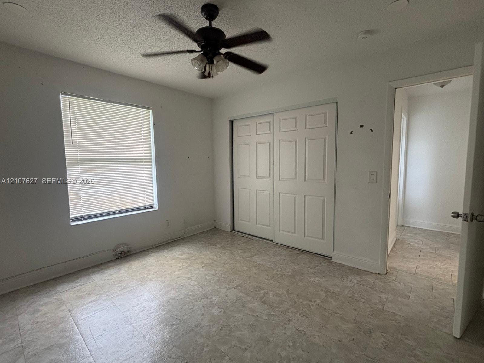 Neutral interior room featuring neutral-toned tile flooring, white walls, a multi-panel sliding closet, and a ceiling fan with integrated lighting