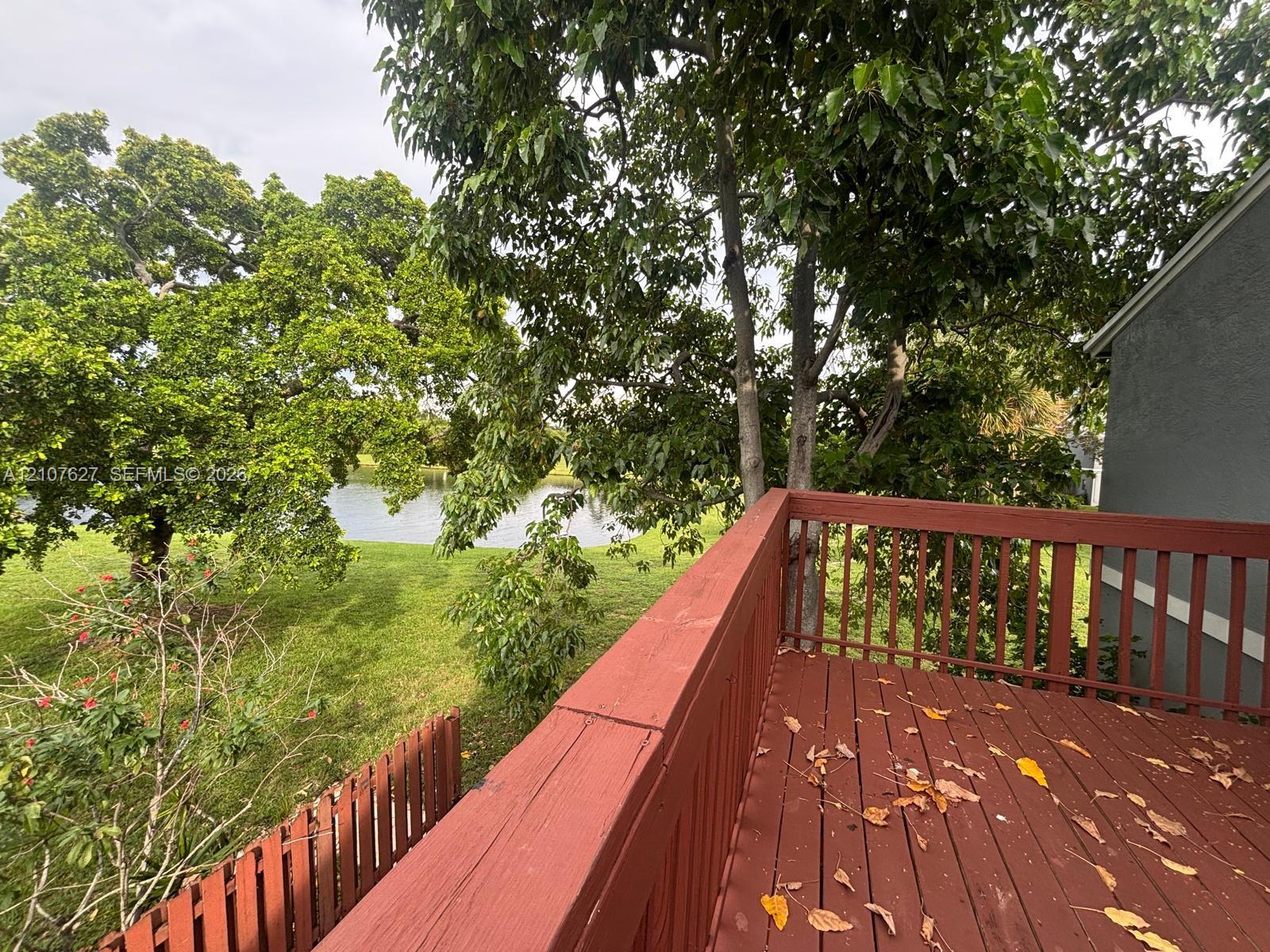 Raised wood deck featuring a railing and open outdoor space, overlooking a pond and mature trees