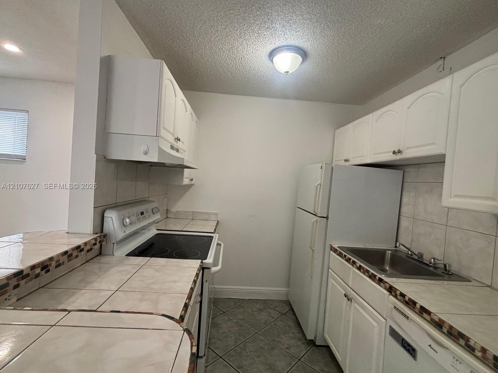 Kitchen featuring white cabinetry, tile countertops with decorative mosaic backsplash, tile flooring, and a stainless steel sink