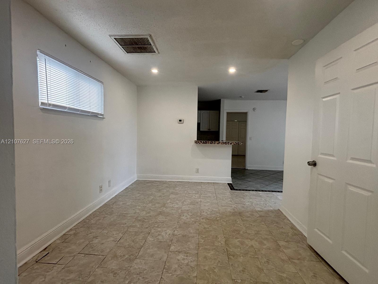 Neutral-toned tile flooring, recessed lighting, horizontal window blinds, and a built-in kitchen pass-through counter