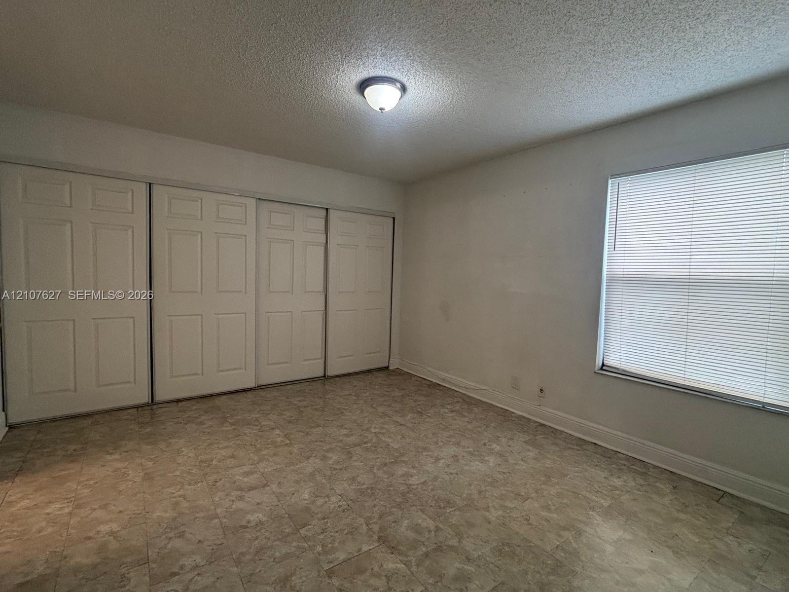 Room featuring tile flooring, four-panel sliding closet doors, and an adjustable window blind