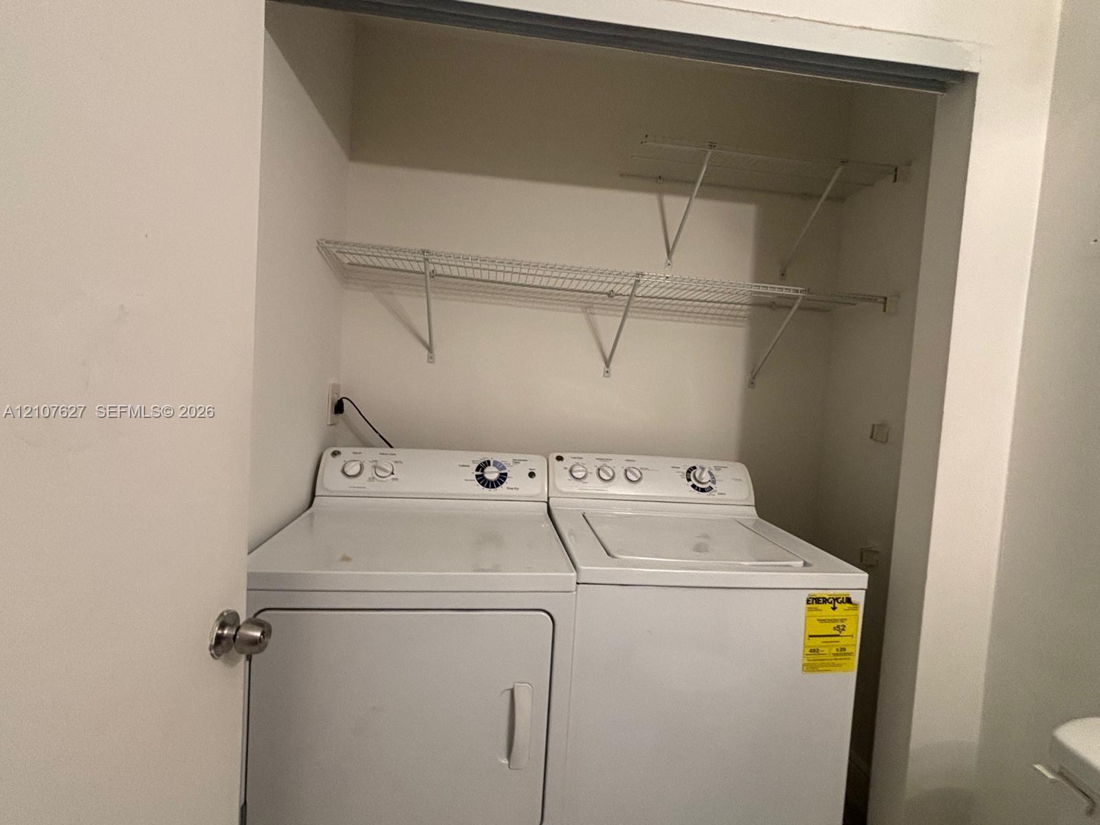Laundry closet featuring white top-load washer and dryer, mounted wire shelving, and neutral wall finish