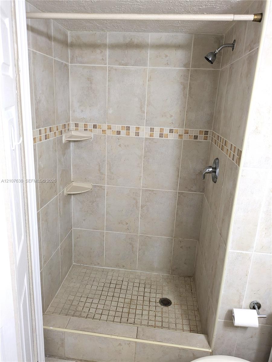Walk-in shower featuring ceramic wall tile, a decorative glass mosaic tile border, integrated corner shelving, and a mosaic tile floor