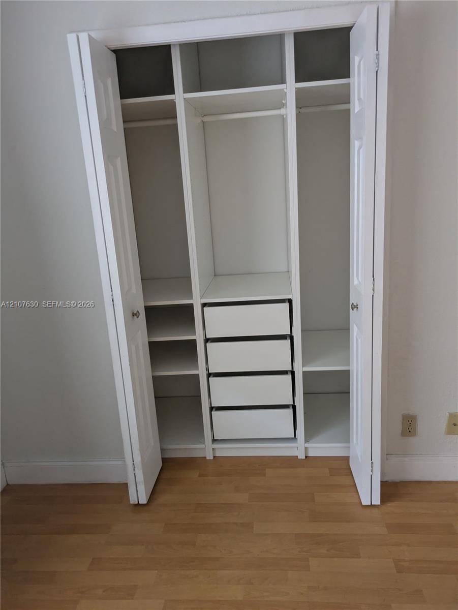 Built-in closet featuring white double-panel doors, integrated shelving, four stacked drawers, and wood-finish flooring