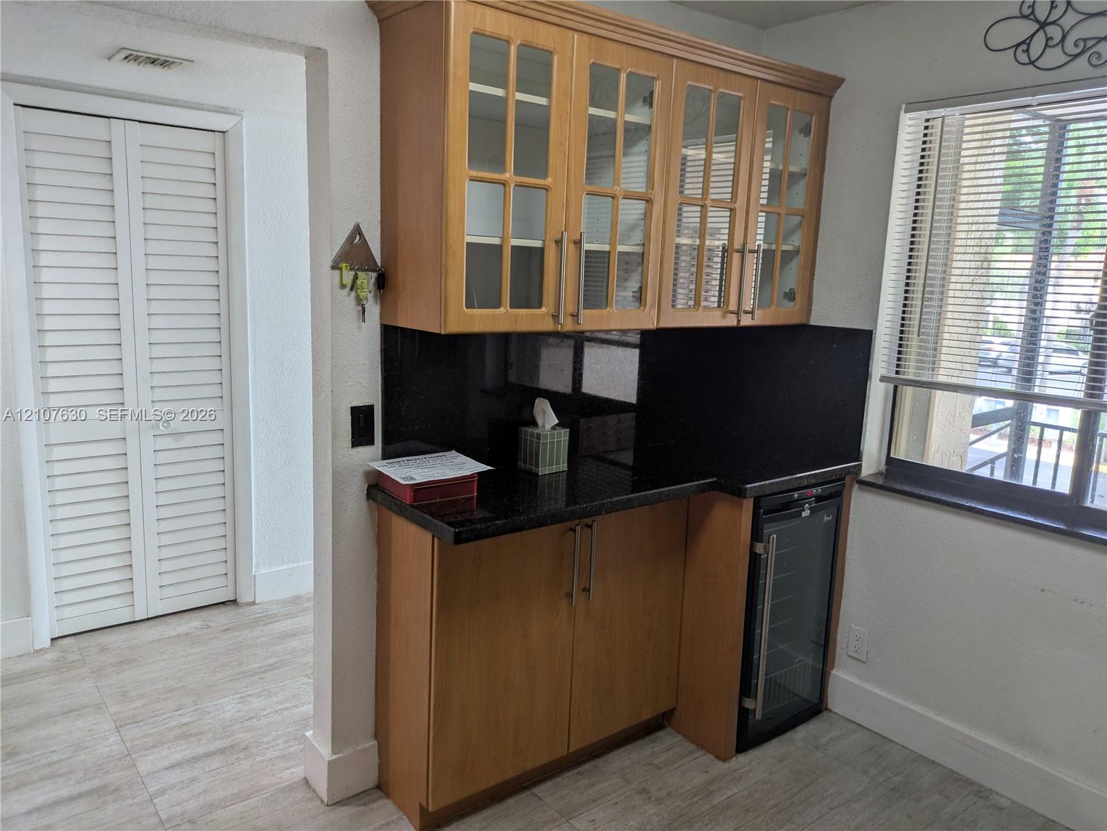 Built-in cabinetry with glass-front upper doors, dark stone-finish countertops, integrated beverage refrigerator, and light wood-finish flooring