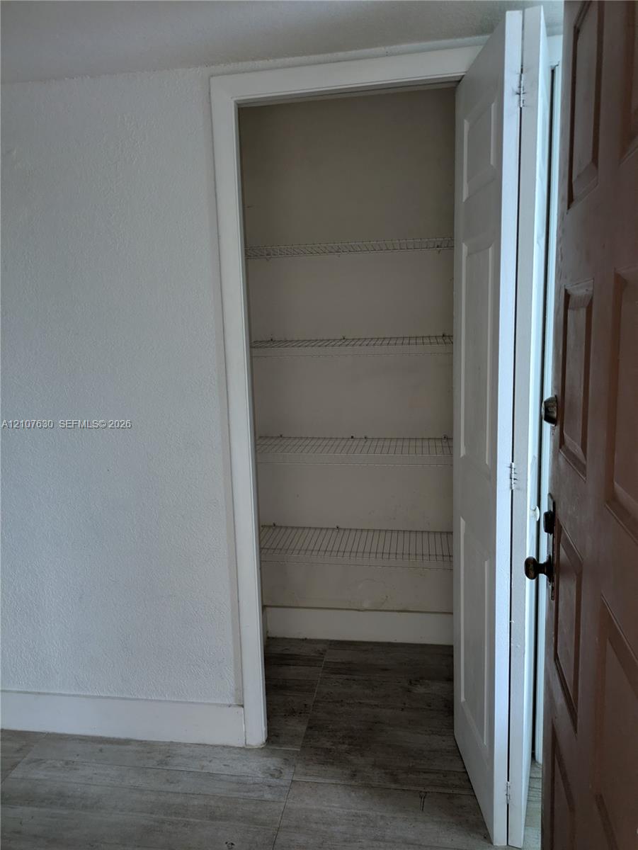 Storage closet featuring multi-tier wire shelving and white paneled door, set against wood-finish flooring