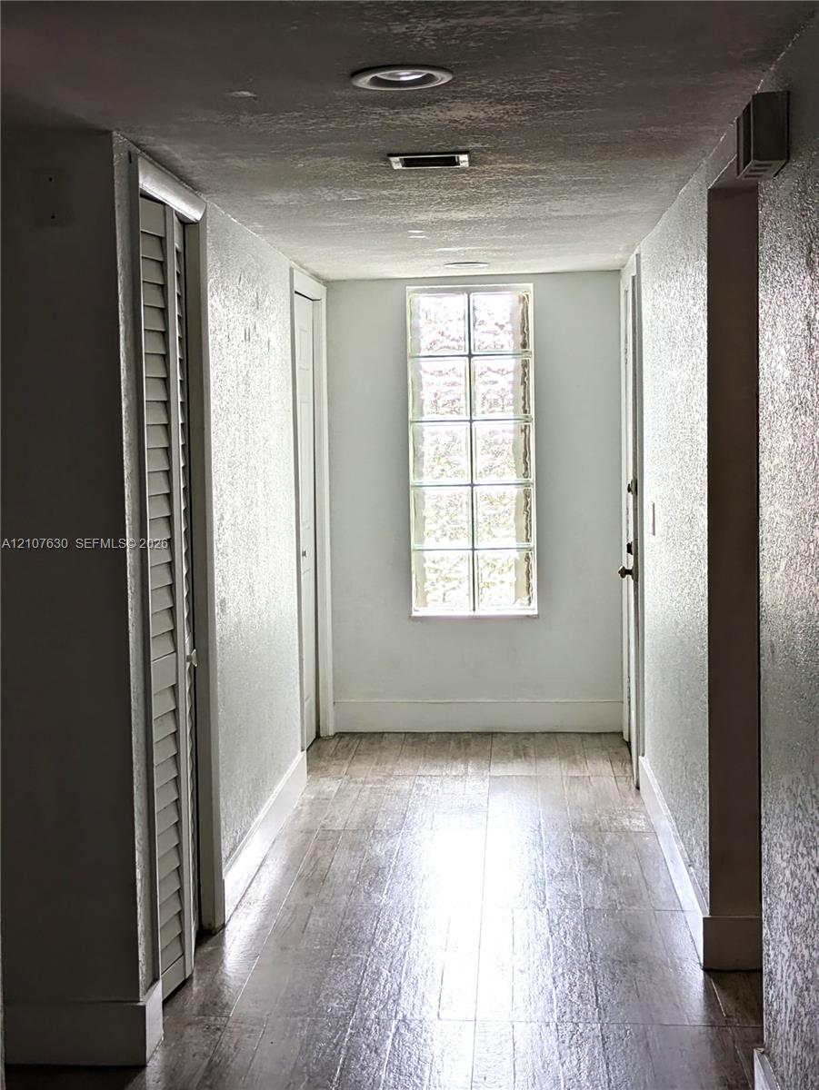 Hallway featuring wood-finish flooring, recessed ceiling lighting, and a multi-pane fixed window with louvered closet doors