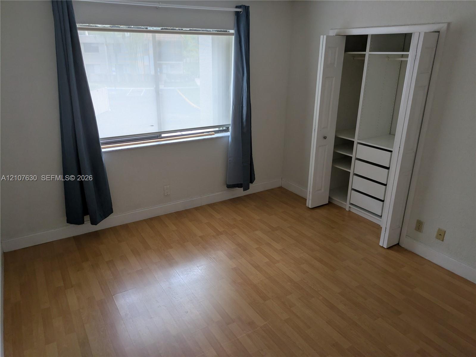 Room featuring wood-finish flooring, a large window, and a built-in closet system with integrated shelving and drawer storage