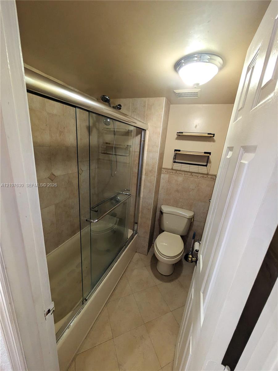 Bathroom featuring a tub-shower combination with glass sliding doors, tile-surround walls, integrated shelving, and wall-mounted storage units