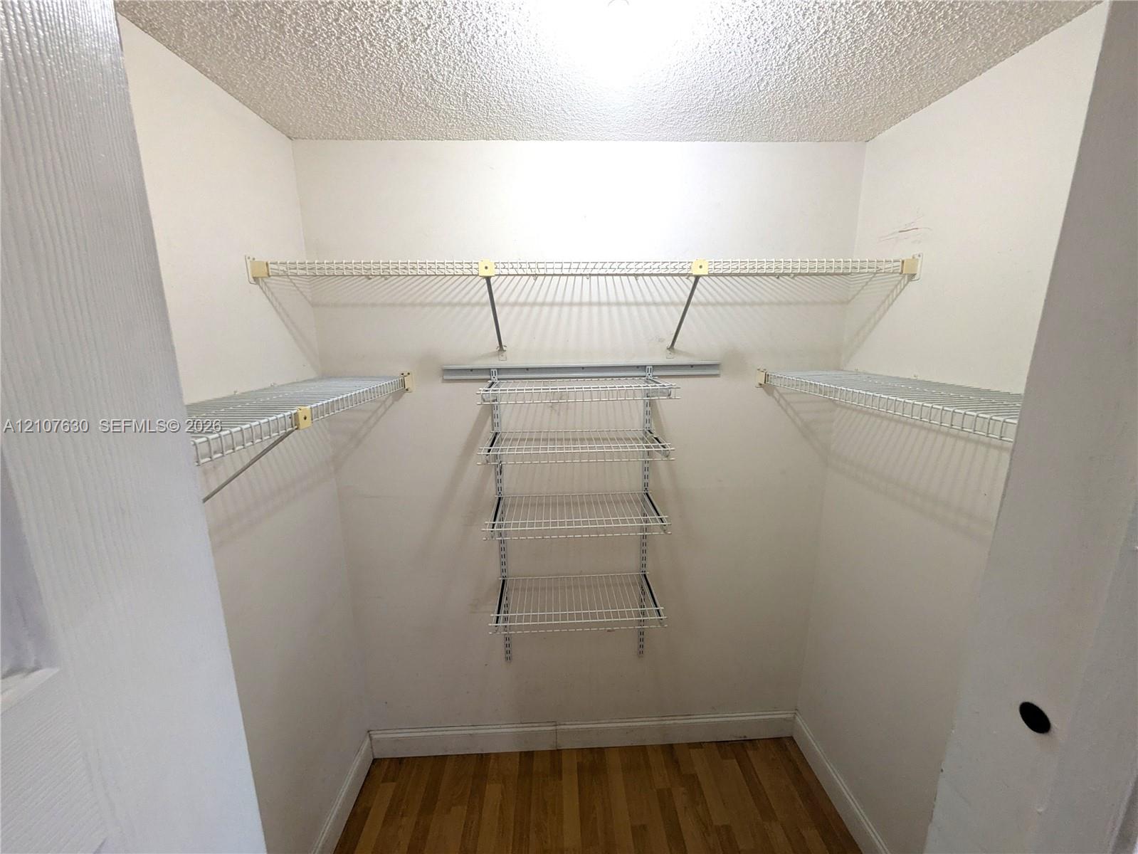 Walk-in closet featuring white wire shelving, a multi-tier hanging organizer, and wood-finish flooring