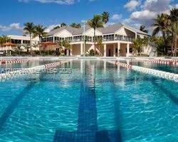 Lap swimming pool with lane markers, surrounded by mature palm trees and multi-level building architecture featuring covered terrace areas