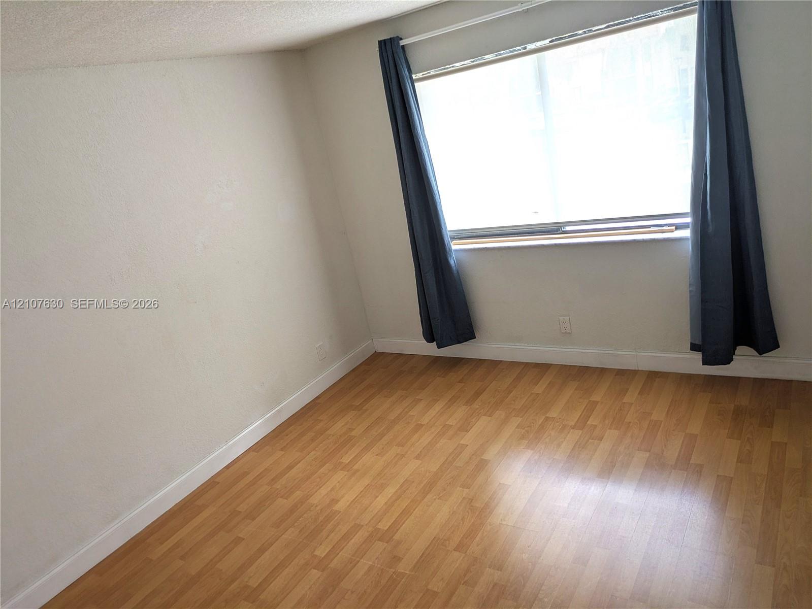 Interior space featuring wood-finish flooring, textured walls, and a window with a horizontal sill