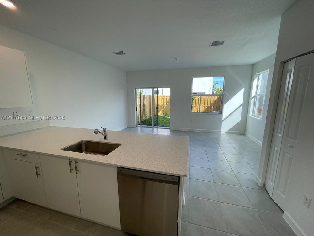 Kitchen featuring an island with a stainless steel undermount sink, quartz countertops, white cabinetry with brushed-metal hardware, stainless steel dishwasher, and tile flooring