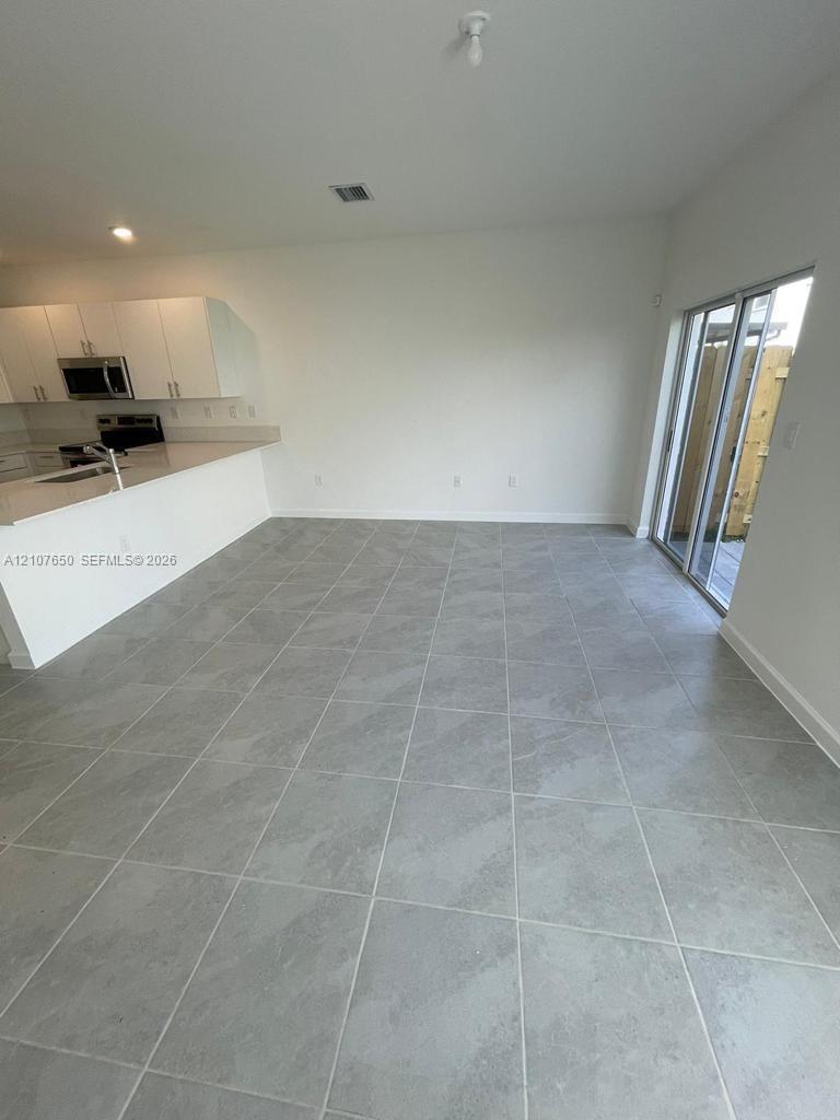 Kitchen featuring white cabinetry, quartz-surface countertops, and built-in stainless steel appliances, complemented by large-format gray tile flooring and sliding glass doors