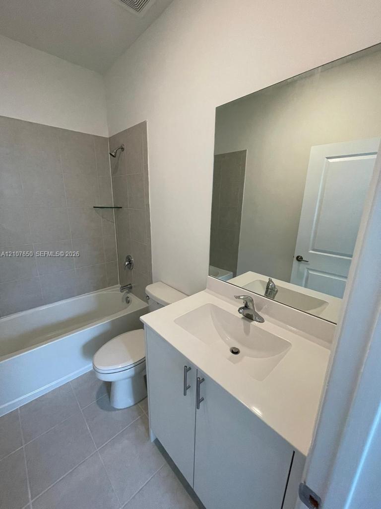 Bathroom featuring a vanity with a white countertop and integrated sink, full-width wall mirror, tile-surround bathtub, and neutral ceramic floor tiling