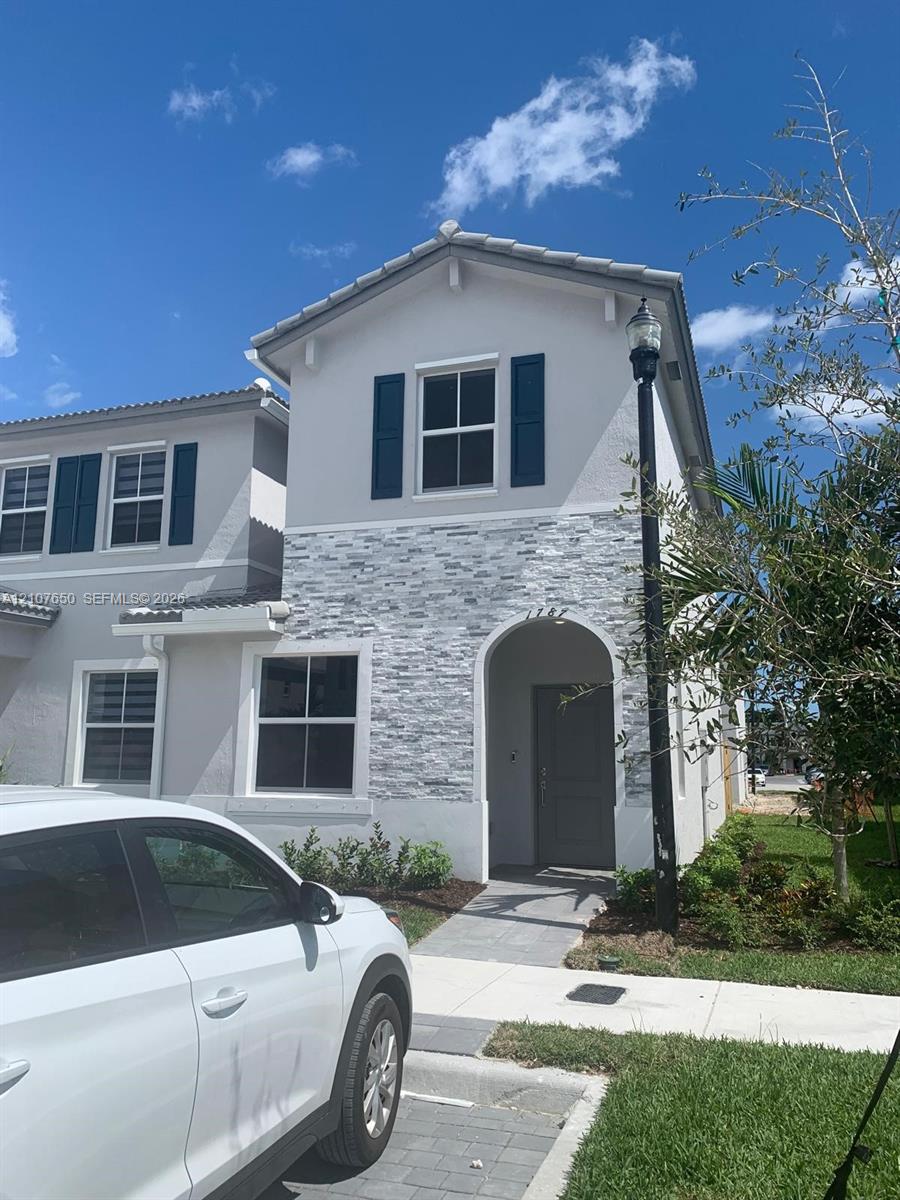 Exterior facade featuring stack stone veneer, arched entryway, dark-toned shutters, tile roof, and paved walkway