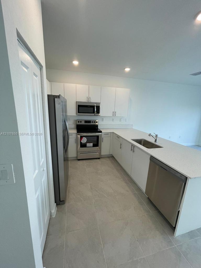 Kitchen featuring white cabinetry, solid-surface countertops, stainless steel appliances, a center island with an undermount sink, and tile flooring