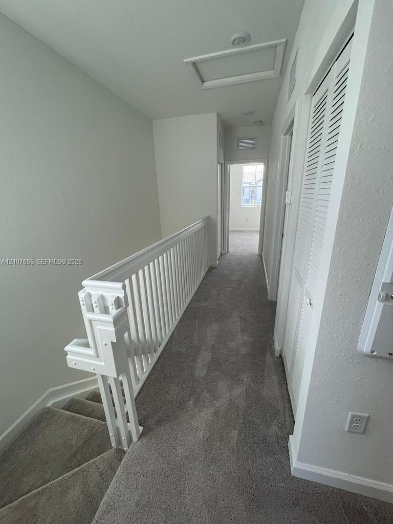 Hallway featuring neutral carpeting, white spindle railing, and louvered closet doors