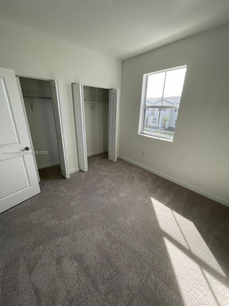 Neutral wall palette, carpeting, dual-door closets with shelving, and window providing natural light