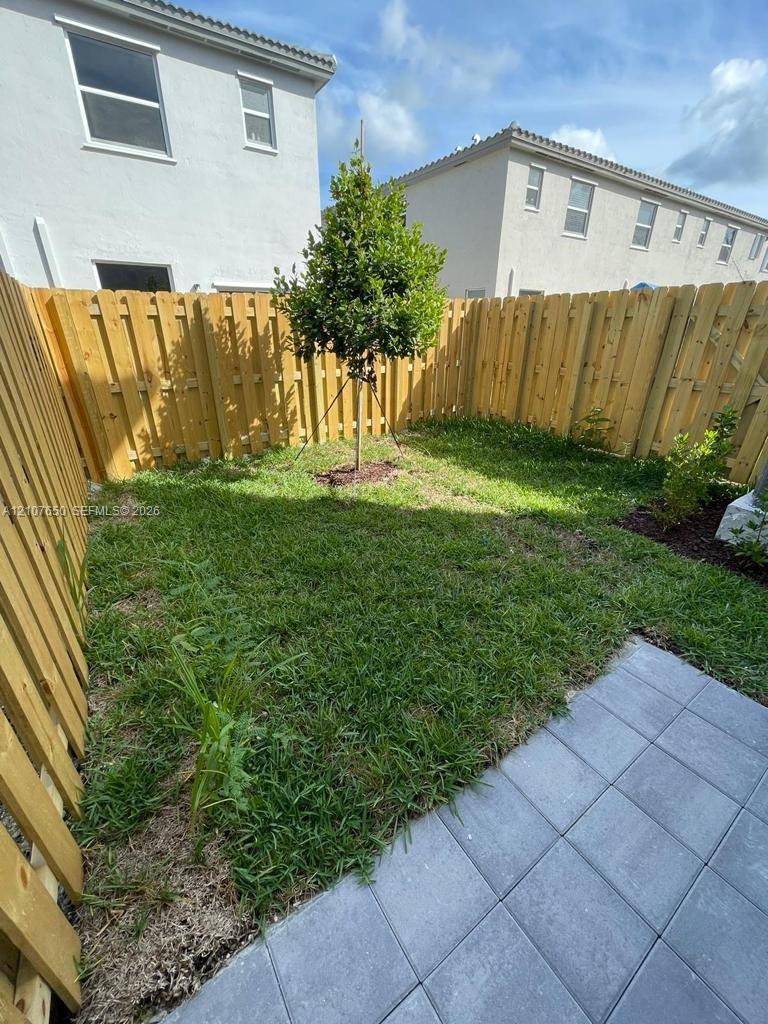 Enclosed outdoor area featuring a wood privacy fence, paved patio, and grass lawn