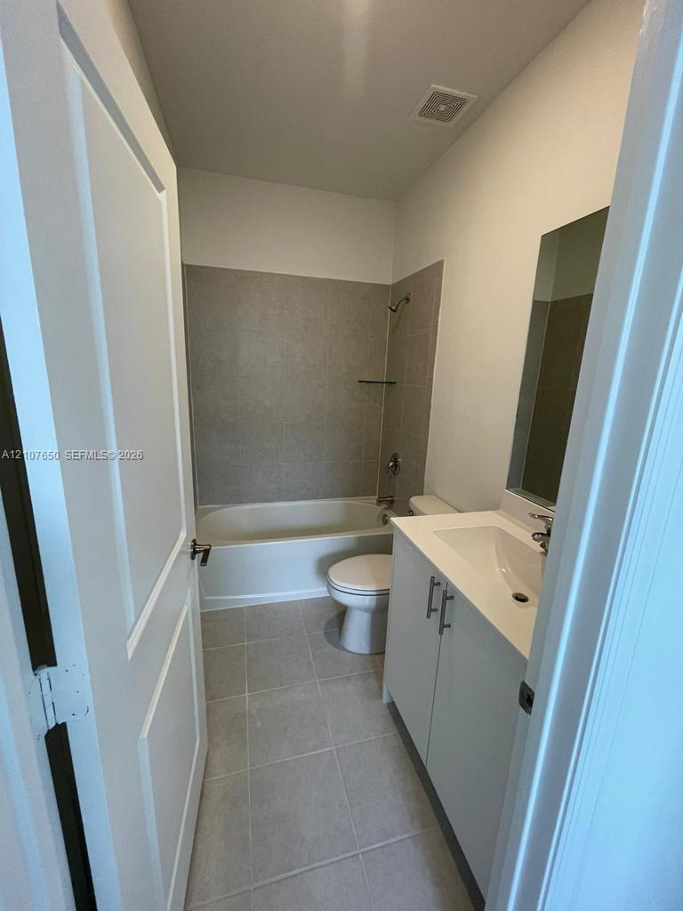 Bathroom featuring a vanity with a solid-surface countertop, tile flooring, and a tub-shower combination with full-height wall tile surrounds