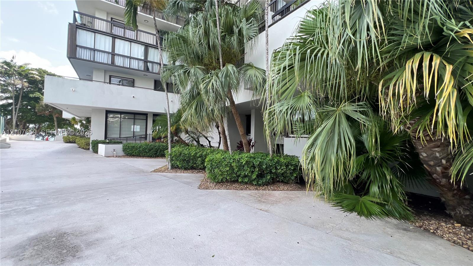 Multi-story building exterior featuring balconies with railings, concrete surfacing, and established palm tree landscaping