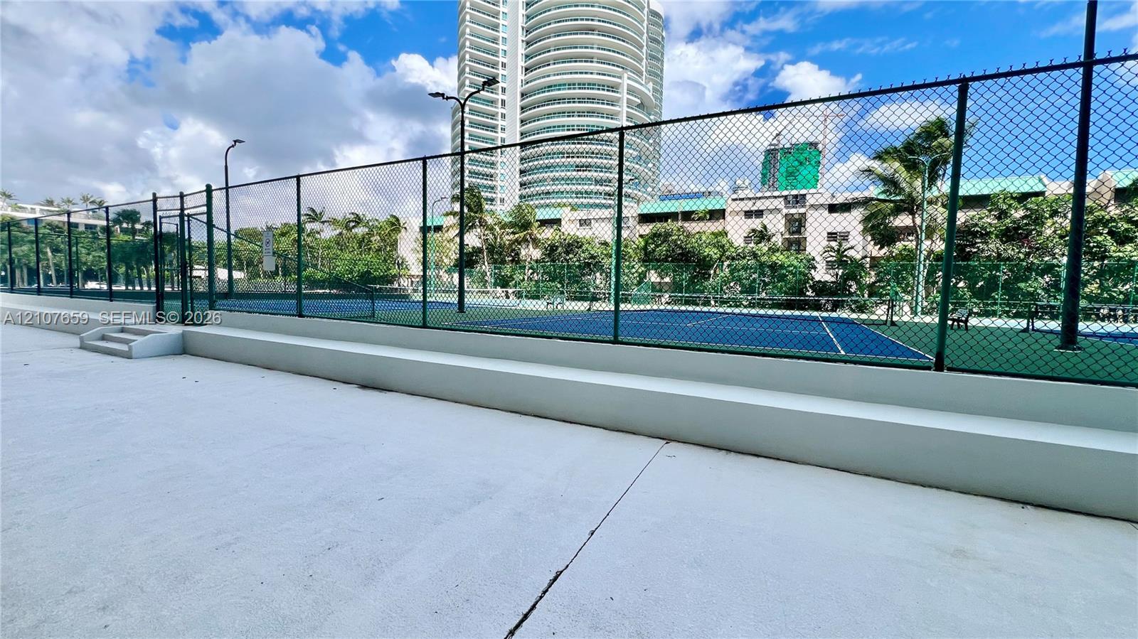 Tennis courts enclosed by chain-link fencing featuring concrete surround, perimeter lighting, and stepped platforms