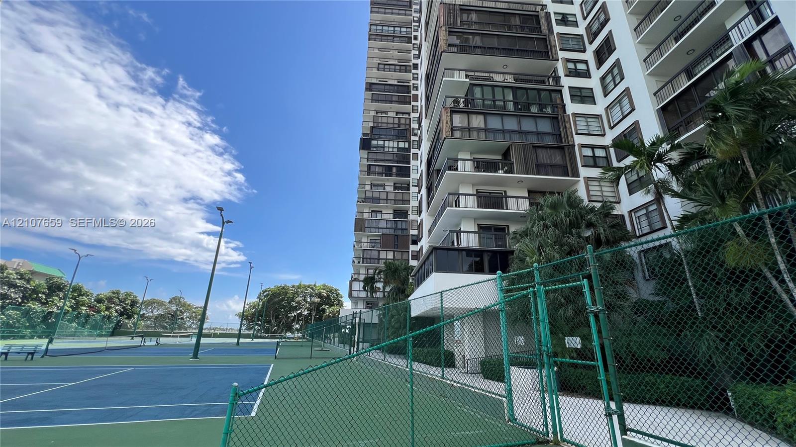 High-rise residential building featuring stacked balconies and a multi-court tennis facility enclosed by chain-link fencing