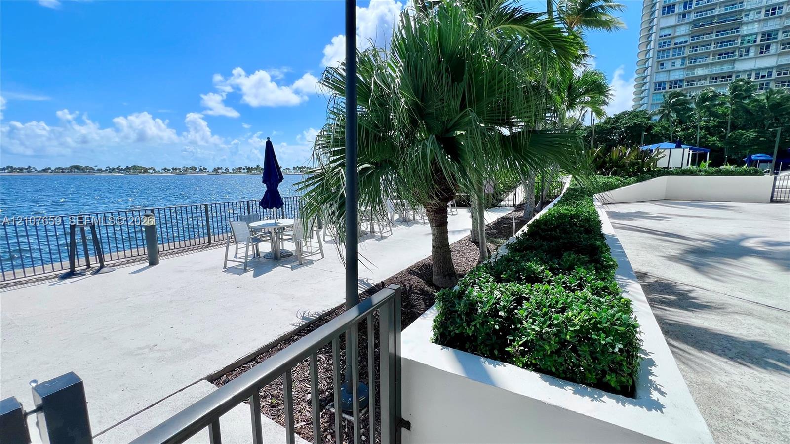 Waterfront concrete patio with metal perimeter fencing, elevated masonry landscape planters, and mature palm trees