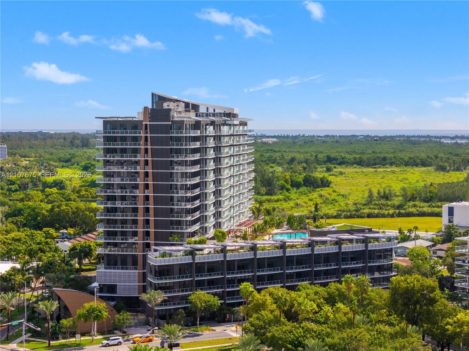 High-rise architectural exterior featuring glass-railed private balconies, multi-story facade, and an elevated outdoor swimming pool with expansive surrounding greenery