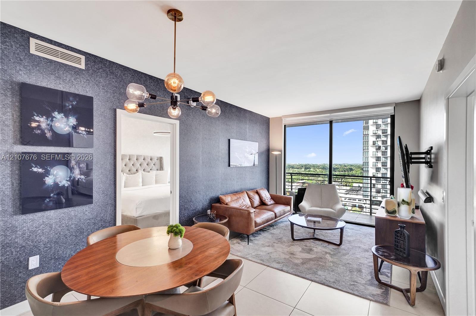 Floor-to-ceiling windows, textured accent wall, multi-light modern chandelier, and tile flooring