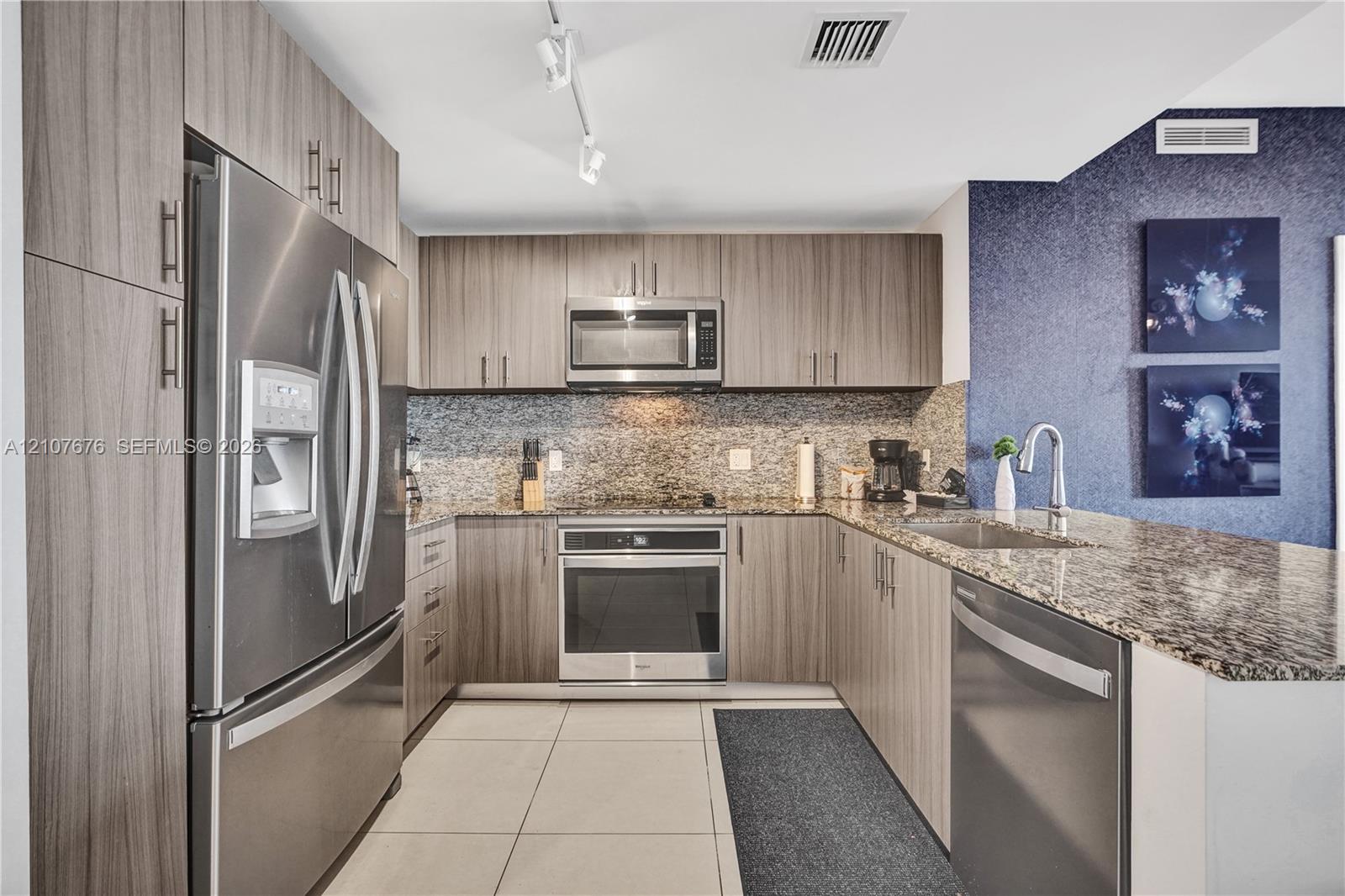 Kitchen featuring wood-finish cabinetry, stainless steel appliances, stone-surface countertops, tile flooring, and track lighting