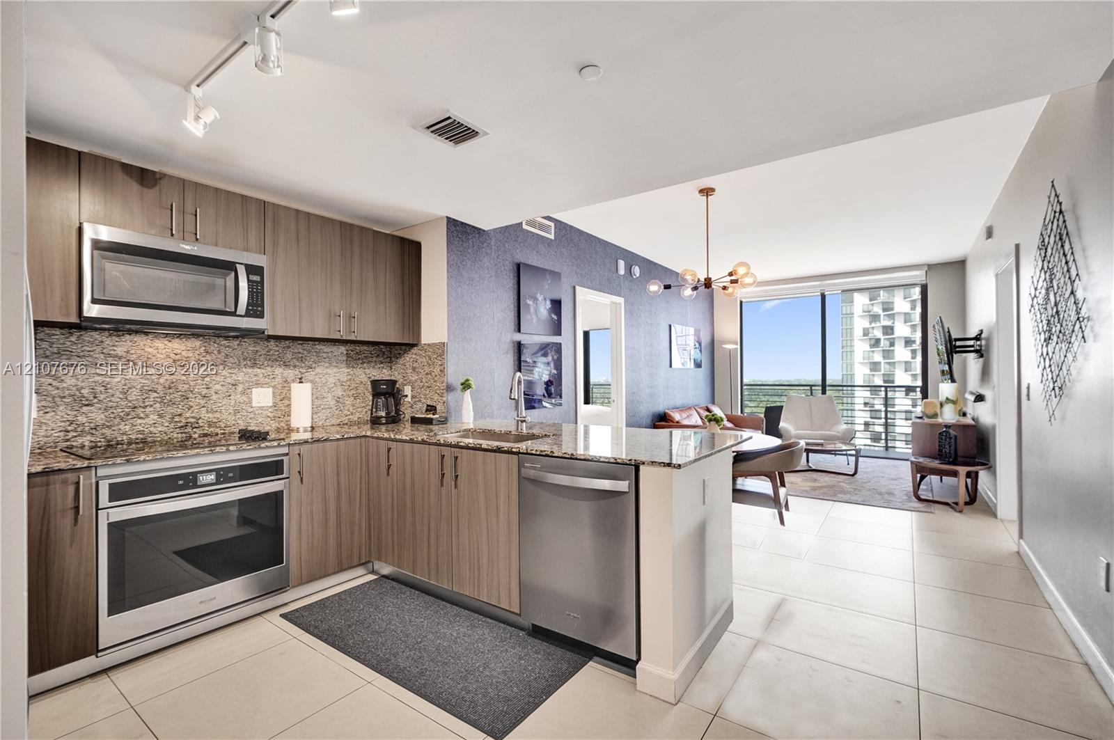 Kitchen featuring wood-finish cabinetry, stone-surface countertops, stainless steel appliances, track lighting, and tile flooring
