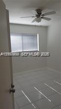 Neutral wall finishes, large-format tile flooring, window with horizontal blinds, and ceiling-mounted fan