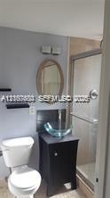 Bathroom featuring a dark wood vanity with a glass vessel sink, oval wall-mounted mirror, two floating wall shelves, and a walk-in shower with a glass enclosure