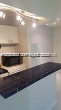 Kitchen featuring white cabinetry, dark tile countertop, and track lighting