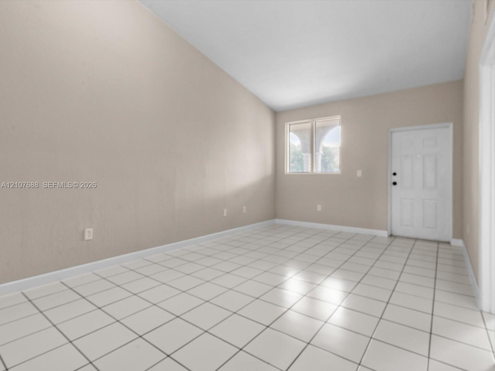 Interior space featuring vaulted ceilings, light-toned ceramic tile flooring, neutral wall paint, and a white six-panel exterior entry door