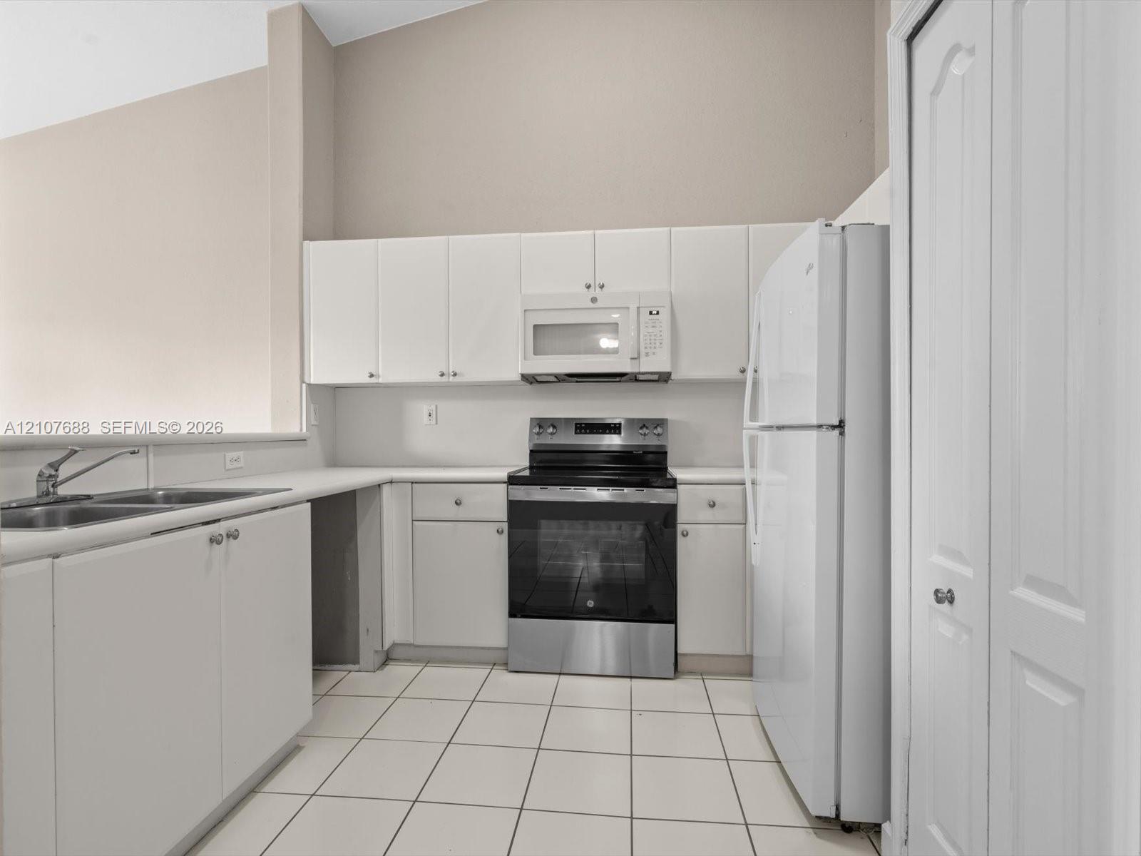 Kitchen featuring white cabinetry, stainless steel oven, white tile flooring, double-basin sink, and vaulted ceiling