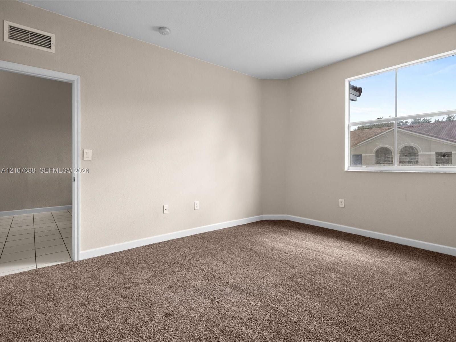 Neutral-toned interior room featuring wall-to-wall carpeting, a single-pane window, and an arched-top doorway leading to a tiled-floor area
