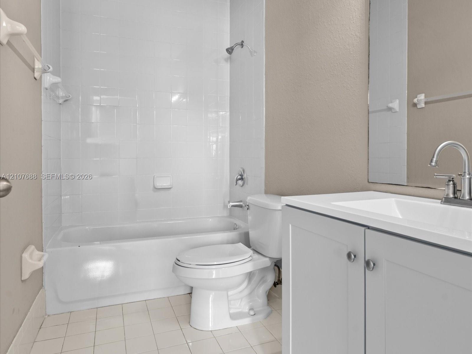 Bathroom featuring a white porcelain tub with tiled surround, a vanity with a white countertop and basin, chrome faucet hardware, and tile flooring