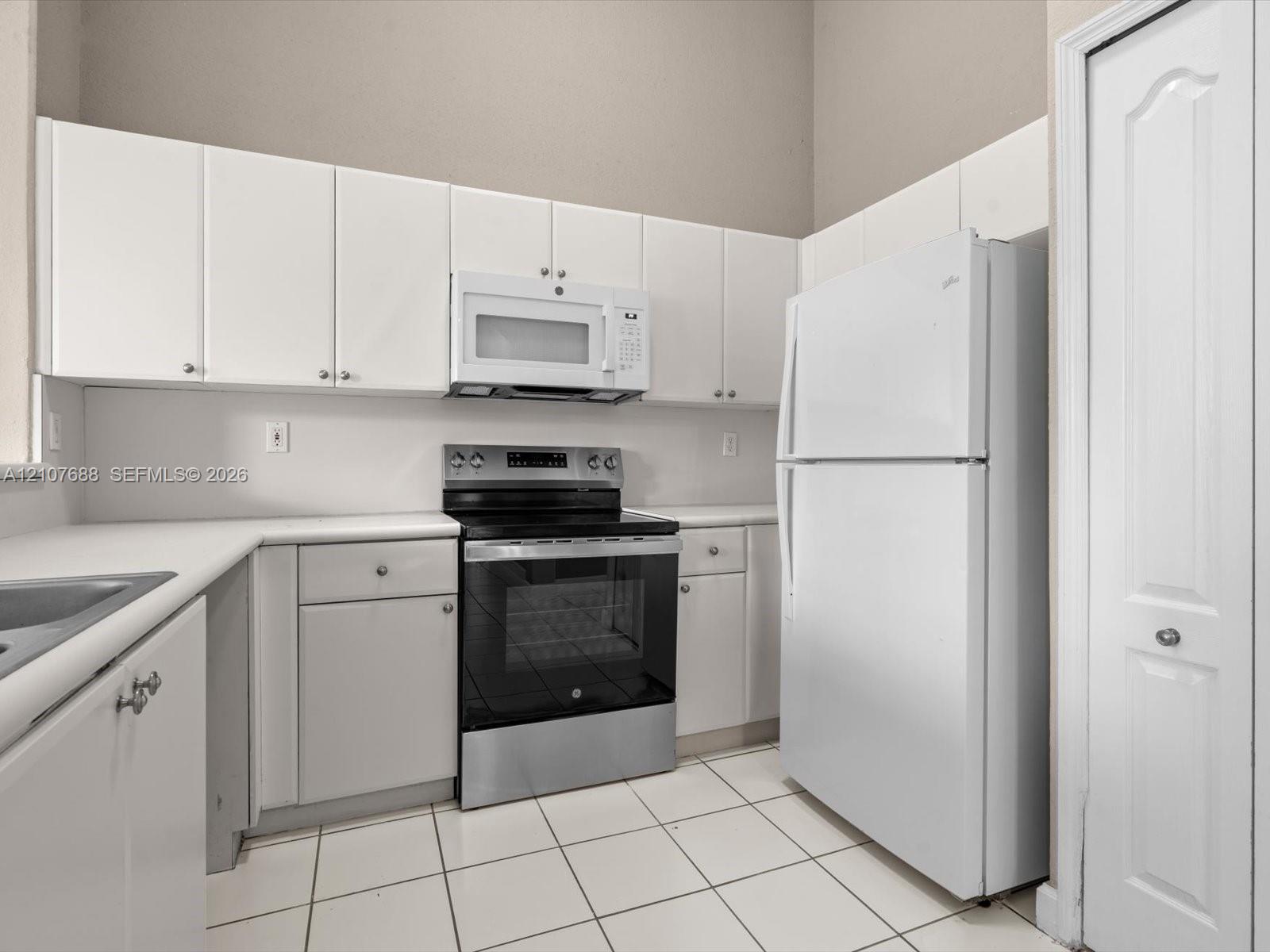 Kitchen featuring white cabinetry, solid-surface countertops, stainless steel range with overhead microwave, white refrigerator, and tile flooring