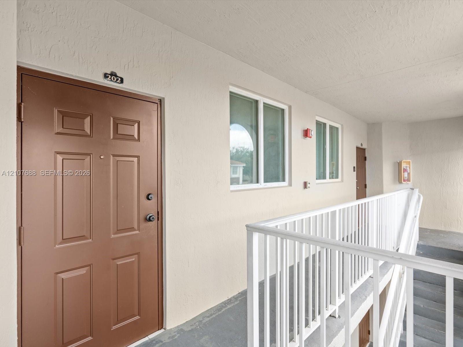 Paneled entry door with hardware, neutral exterior wall finish, white metal railing, and dual-pane windows