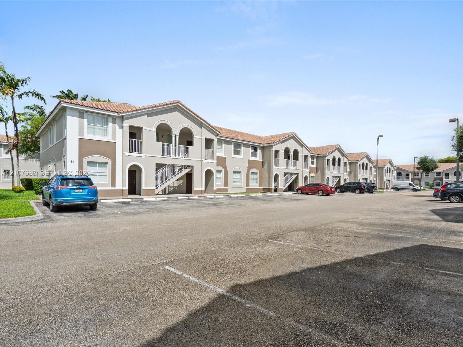 Two-story building featuring stucco exterior, clay tile roof, arched entryway accents, and dedicated surface parking