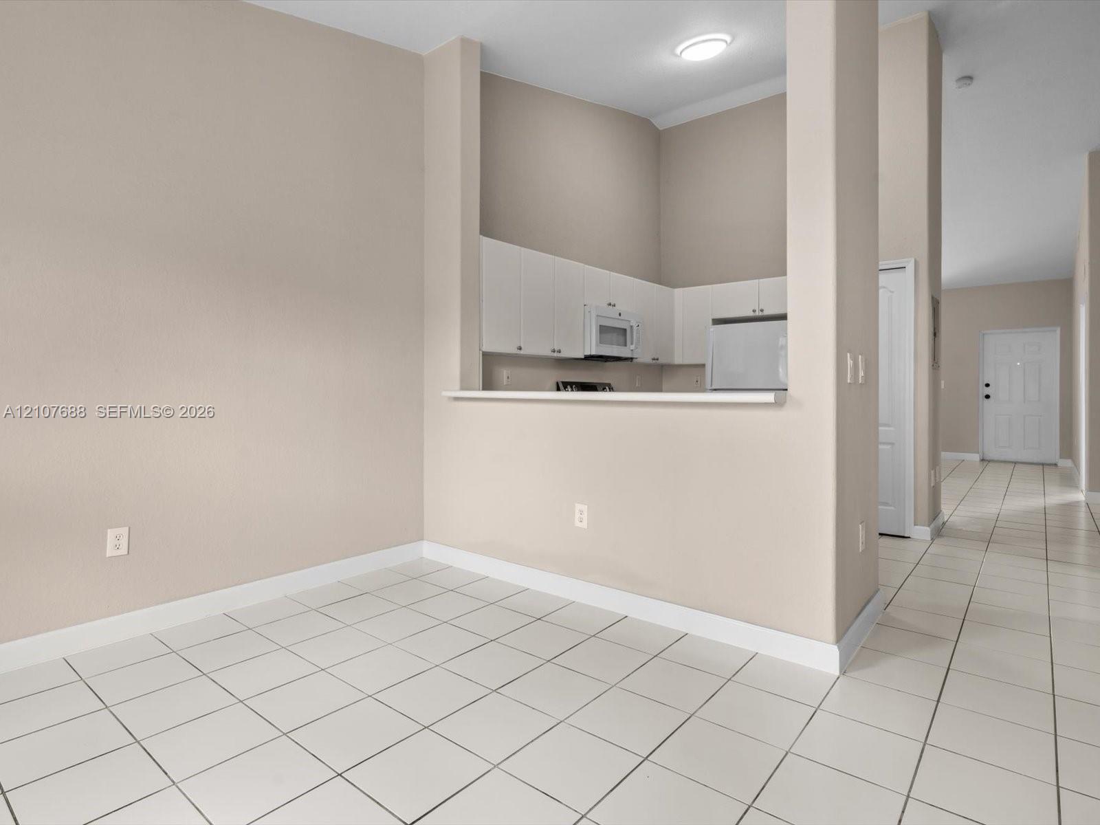 Kitchen featuring white cabinetry, an integrated microwave, and a pass-through counter, with ceramic tile flooring throughout