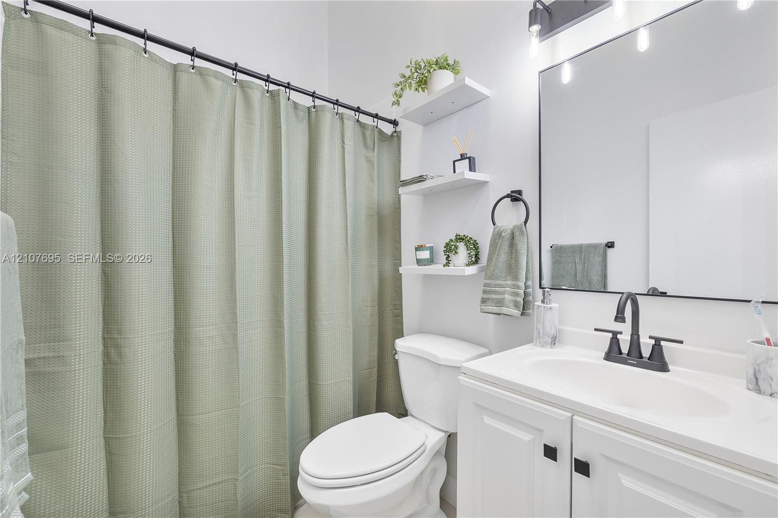 Bathroom featuring a white vanity with a rectangular sink, matte black faucet, wall-mounted light fixture with glass shades, frameless mirror, and built-in shelving